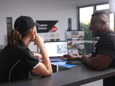 Two people leaning on a counter looking at a website on a laptop